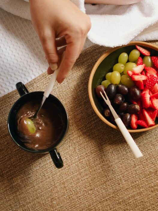 Top view of a delicious fruit and chocolate fondue setup with strawberries, grapes, and dipping cup.