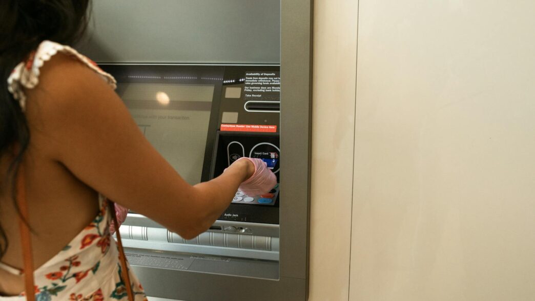 Woman using an ATM machine while wearing protective gloves indoors.