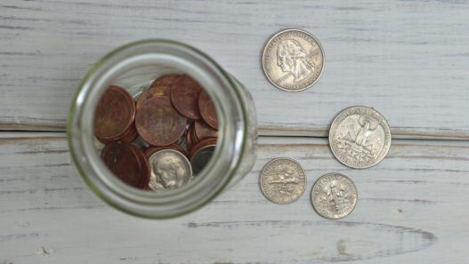 Top view of a jar filled with coins placed on a wooden table, depicting savings.