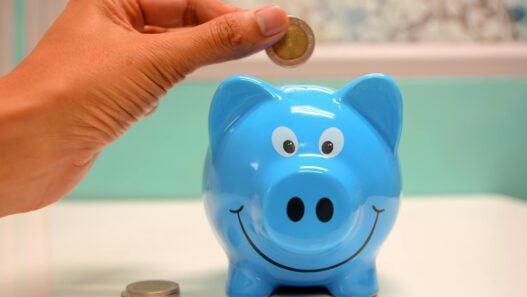 Hand inserting a coin into a blue piggy bank for savings and money management.