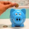 Hand inserting a coin into a blue piggy bank for savings and money management.