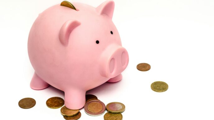 A pink piggy bank surrounded by scattered coins, symbolizing savings and financial investment.