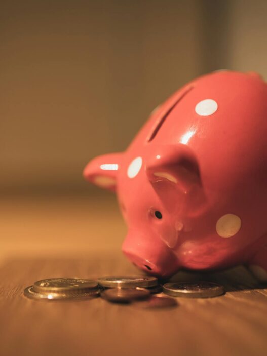 A red ceramic piggy bank with polka dots surrounded by coins, symbolizing savings and finance.