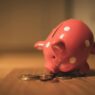 A red ceramic piggy bank with polka dots surrounded by coins, symbolizing savings and finance.