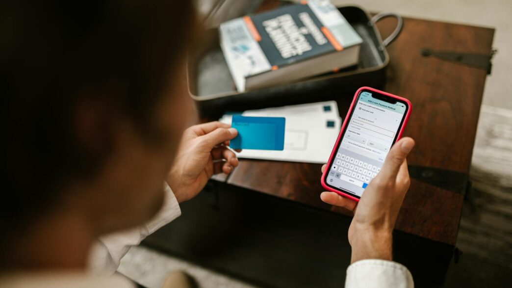 Person making an online payment using a smartphone and credit card indoors.