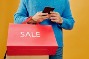 Person using a smartphone for online shopping with shopping bags nearby, illustrating cash back apps