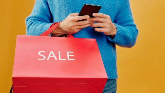 Person using a smartphone for online shopping with shopping bags nearby, illustrating cash back apps