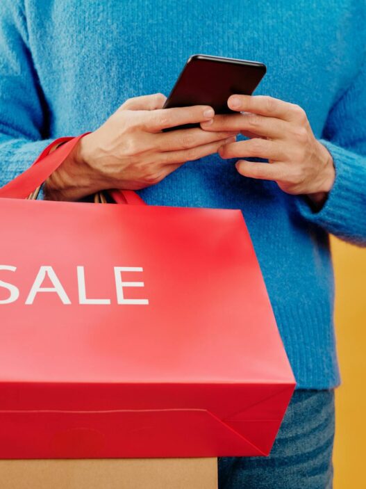 Person using a smartphone for online shopping with shopping bags nearby, illustrating cash back apps