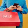 Person using a smartphone for online shopping with shopping bags nearby, illustrating cash back apps