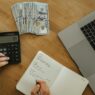 Notebook, calculator, and coffee on a desk during a mid-year personal finance review