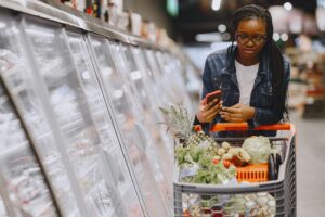 A shopper using a smartphone while grocery shopping, illustrating coupon stacking apps to save money in 2026