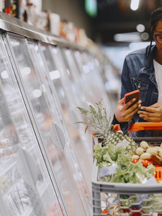A shopper using a smartphone while grocery shopping, illustrating coupon stacking apps to save money in 2026