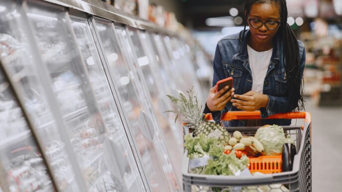 A shopper using a smartphone while grocery shopping, illustrating coupon stacking apps to save money in 2026