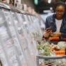 A shopper using a smartphone while grocery shopping, illustrating coupon stacking apps to save money in 2026