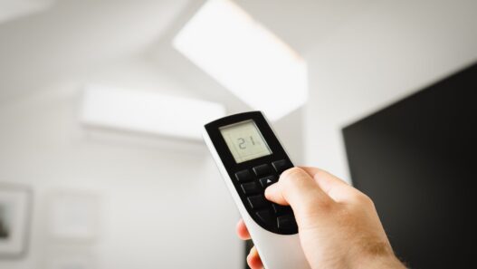 Hand adjusting a home thermostat to cut summer air conditioning costs