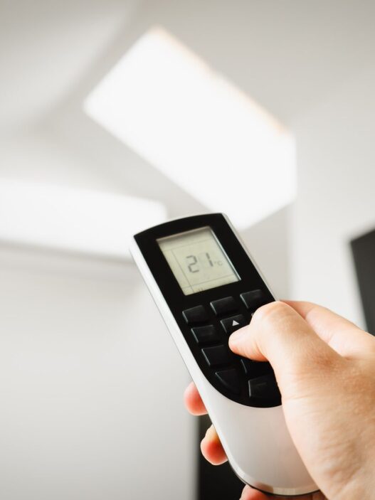 Hand adjusting a home thermostat to cut summer air conditioning costs