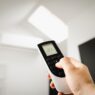 Hand adjusting a home thermostat to cut summer air conditioning costs