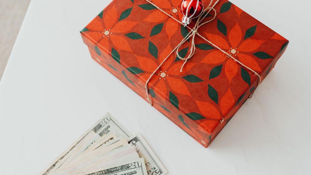 Wrapped holiday gifts beside cash and a savings envelope for a holiday sinking fund