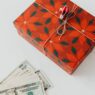 Wrapped holiday gifts beside cash and a savings envelope for a holiday sinking fund