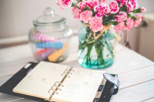A monthly calendar and notebook beside a jar of coins on a desk