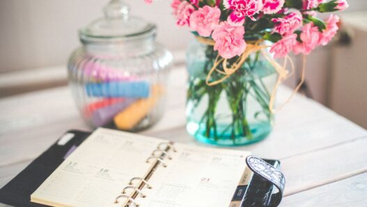 A monthly calendar and notebook beside a jar of coins on a desk