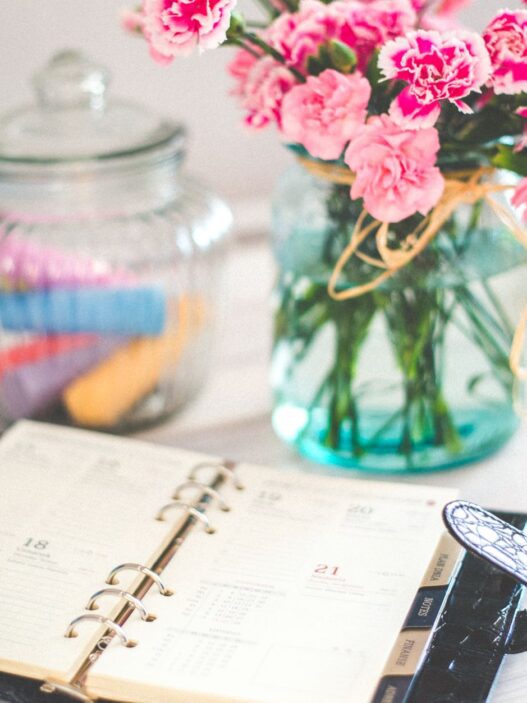 A monthly calendar and notebook beside a jar of coins on a desk