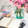 A monthly calendar and notebook beside a jar of coins on a desk