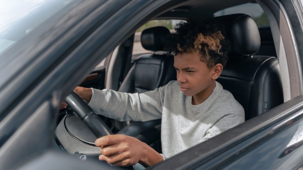 A young driver behind the wheel of a car, illustrating the cost of adding a teen driver to an auto policy