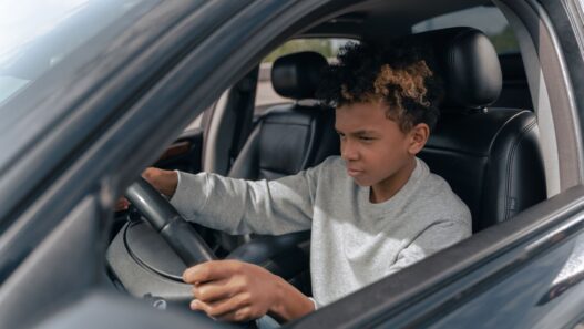 A young driver behind the wheel of a car, illustrating the cost of adding a teen driver to an auto policy