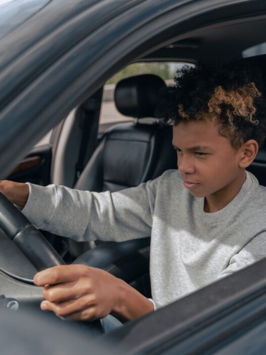 A young driver behind the wheel of a car, illustrating the cost of adding a teen driver to an auto policy