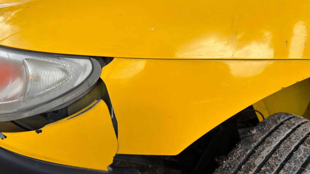 A damaged car bumper being inspected at a body shop, illustrating car insurance deductible costs