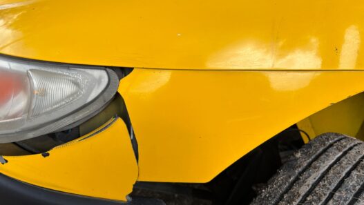 A damaged car bumper being inspected at a body shop, illustrating car insurance deductible costs