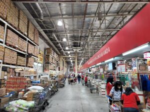 A shopping cart loaded with bulk groceries inside a warehouse club store
