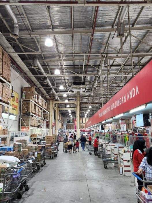 A shopping cart loaded with bulk groceries inside a warehouse club store