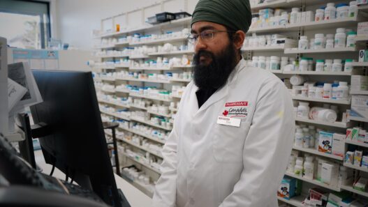A pharmacist handling a prescription at the counter, illustrating formulary and tiering exception requests
