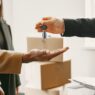 Renter holding apartment keys next to moving boxes in an empty apartment
