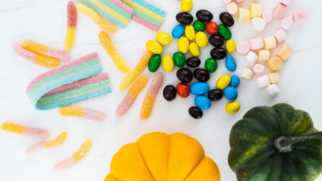 Bowl of wrapped Halloween candy next to small pumpkins on a table