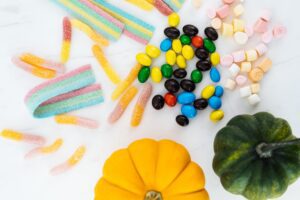 Bowl of wrapped Halloween candy next to small pumpkins on a table