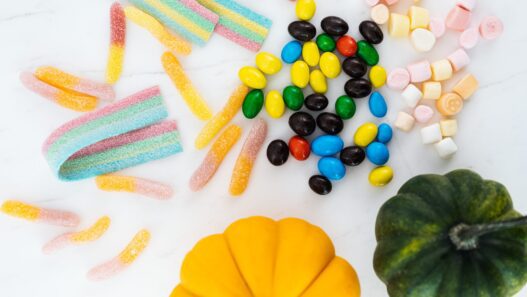 Bowl of wrapped Halloween candy next to small pumpkins on a table