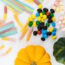 Bowl of wrapped Halloween candy next to small pumpkins on a table