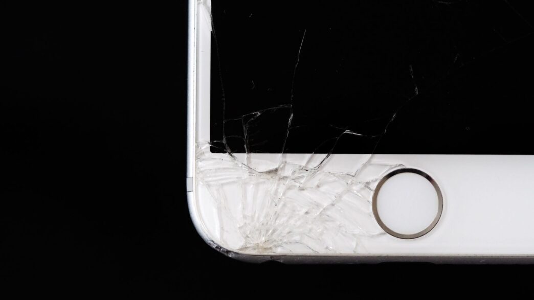 A smartphone with a cracked screen resting on a desk