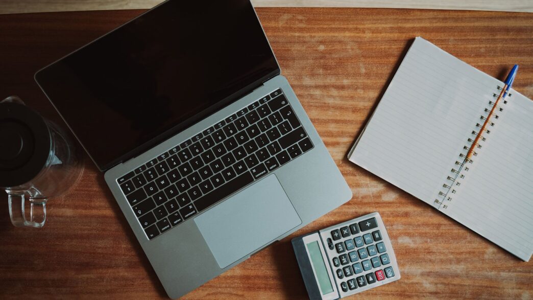 Person paying household bills online at a laptop next to a calculator