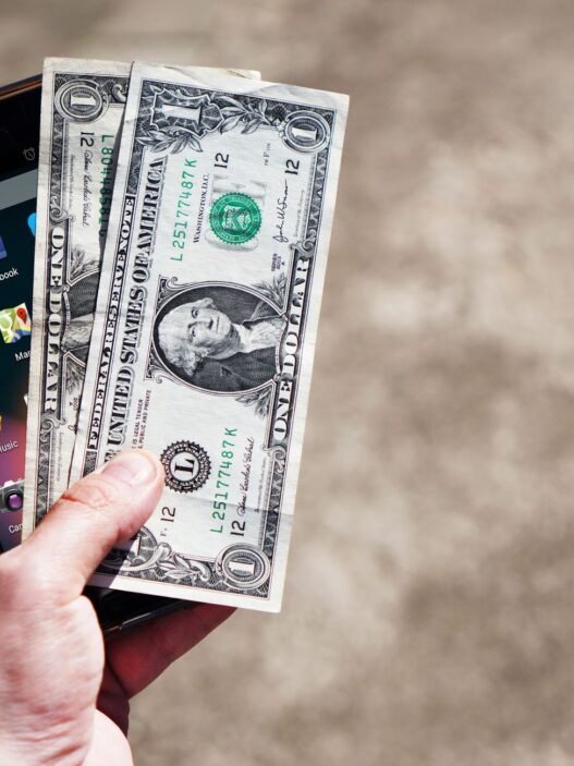 Hand holding cash and a smartphone, illustrating earned wage access pay apps and their fees