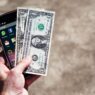 Hand holding cash and a smartphone, illustrating earned wage access pay apps and their fees