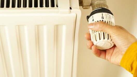 Hand turning a radiator valve, illustrating winter heating costs and utility budget billing