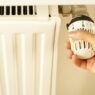 Hand turning a radiator valve, illustrating winter heating costs and utility budget billing